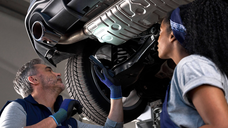 Two VW technicians inspecting the underside of a VW vehicle. 