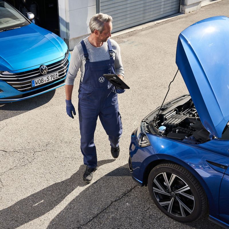 Un empleado del servicio técnico de VW ante un capó abierto: revisión de un vehículo VW