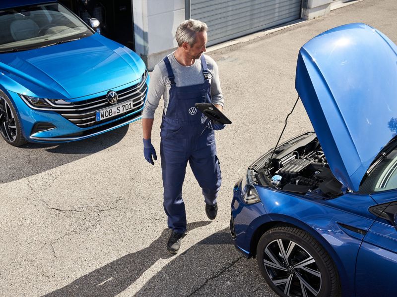 Un collaborateur de service se tient devant une VW dans l’atelier et effectue une inspection