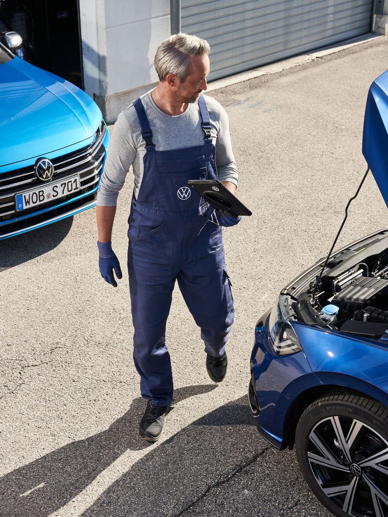 A VW service employee refills Volkswagen Genuine Engine Oil while the inspection in a yellow Golf