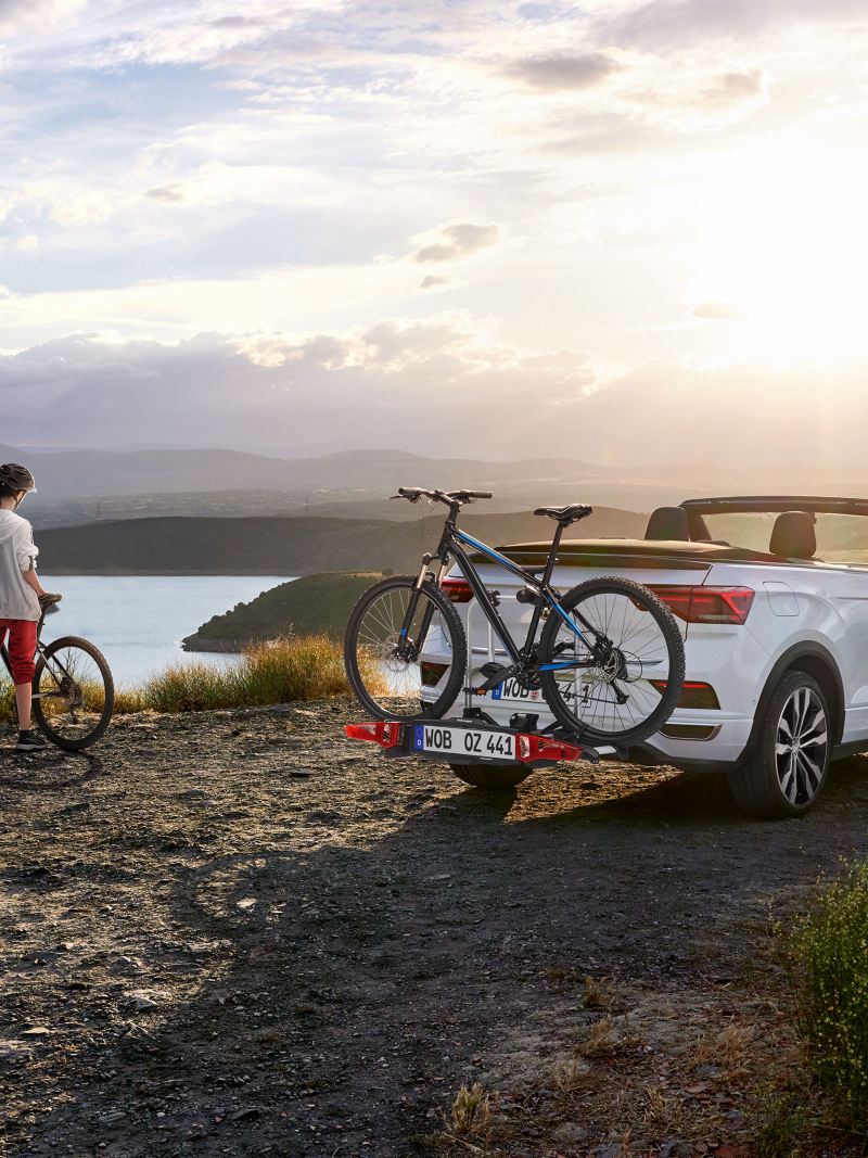 Eine Frau mit einem Fahrrad neben ihrem VW T-Roc Cabriolet mit Fahrradträger