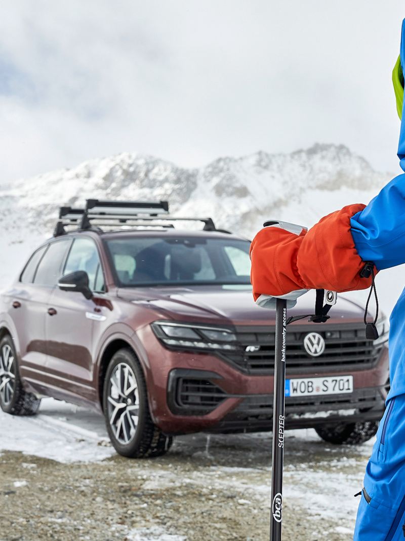 Ein Mann auf Skiern vor seinem VW Auto in einer verschneiten Landschaft
