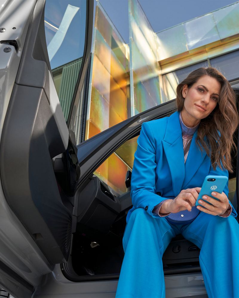 Eine Frau mit einem Smartphone in der Hand sitzt in einem VW Auto