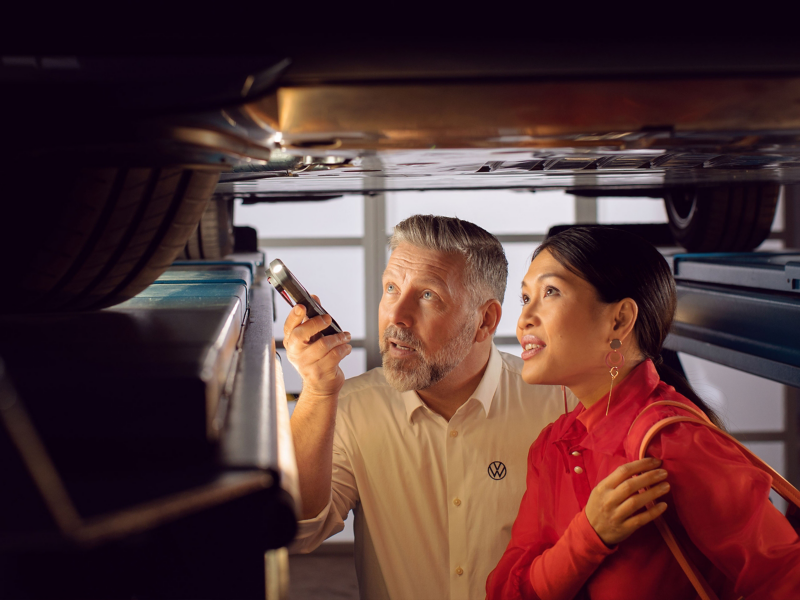 VW service worker and woman look at underbody of a Volkswagen at the lifting platform