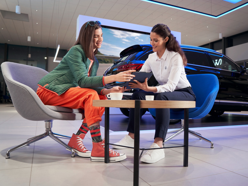 VW service employee and customer looking at a tablet together, a VW car in the background