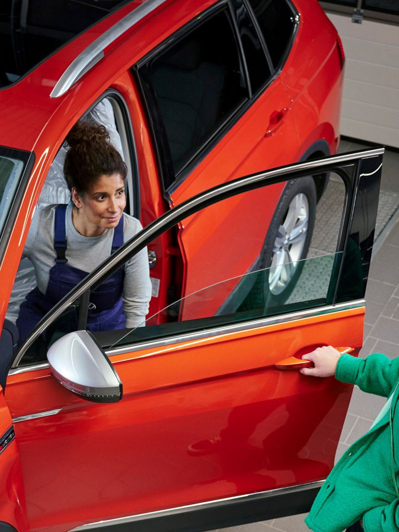 Eine Servicemitarbeiterin steigt nach dem Fahrzeug Check aus einem VW Tiguan, ein Kunde öffnet ihr die Tür