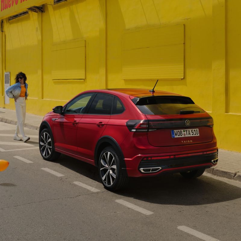 VW Taigo in Rot am Straßenrand vor Gebäude, eine Frau geht auf das Fahrzeug zu