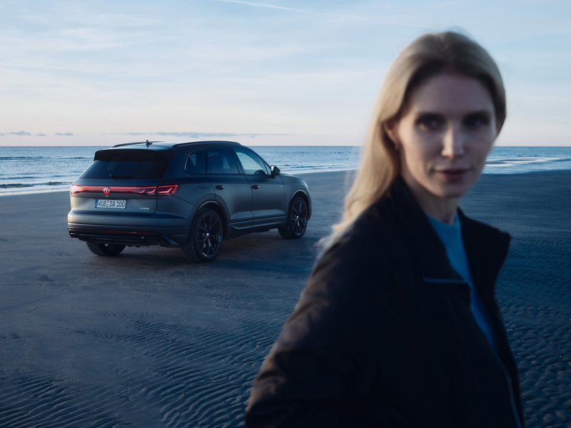 VW Touareg R FINAL EDITION am Strand, im Vordergrund eine Frau, im Hintergrund das Meer