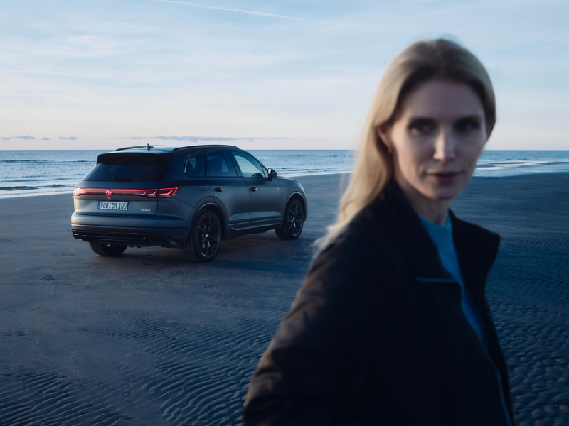 VW Touareg R FINAL EDITION am Strand, im Vordergrund eine Frau, im Hintergrund das Meer