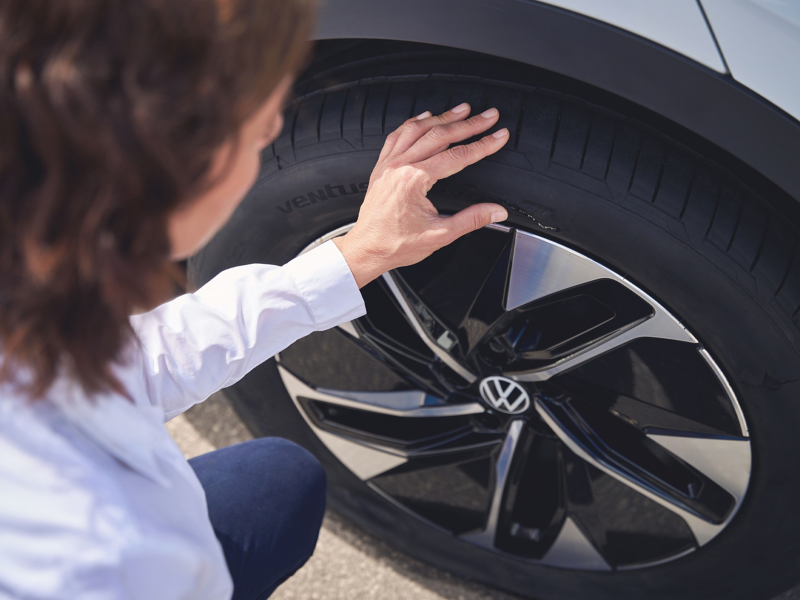 VW Servicemitarbeiterin hält Hand an Reifen eines VW ID.4 Pro und prüft diesen auf Schäden