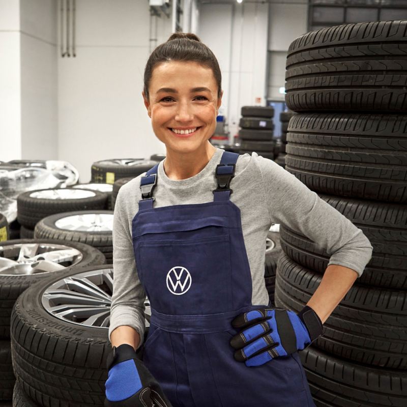 A smiling VW service employee with a stack of tyres behind her