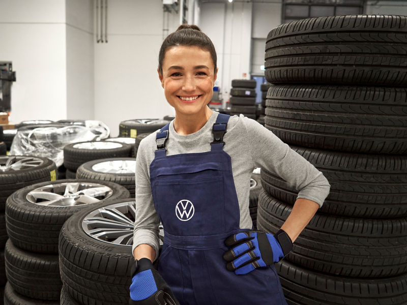 A smiling VW service employee with a stack of tyres behind her