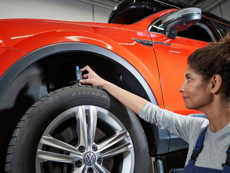 A VW service expert using a measuring tool on a tyre