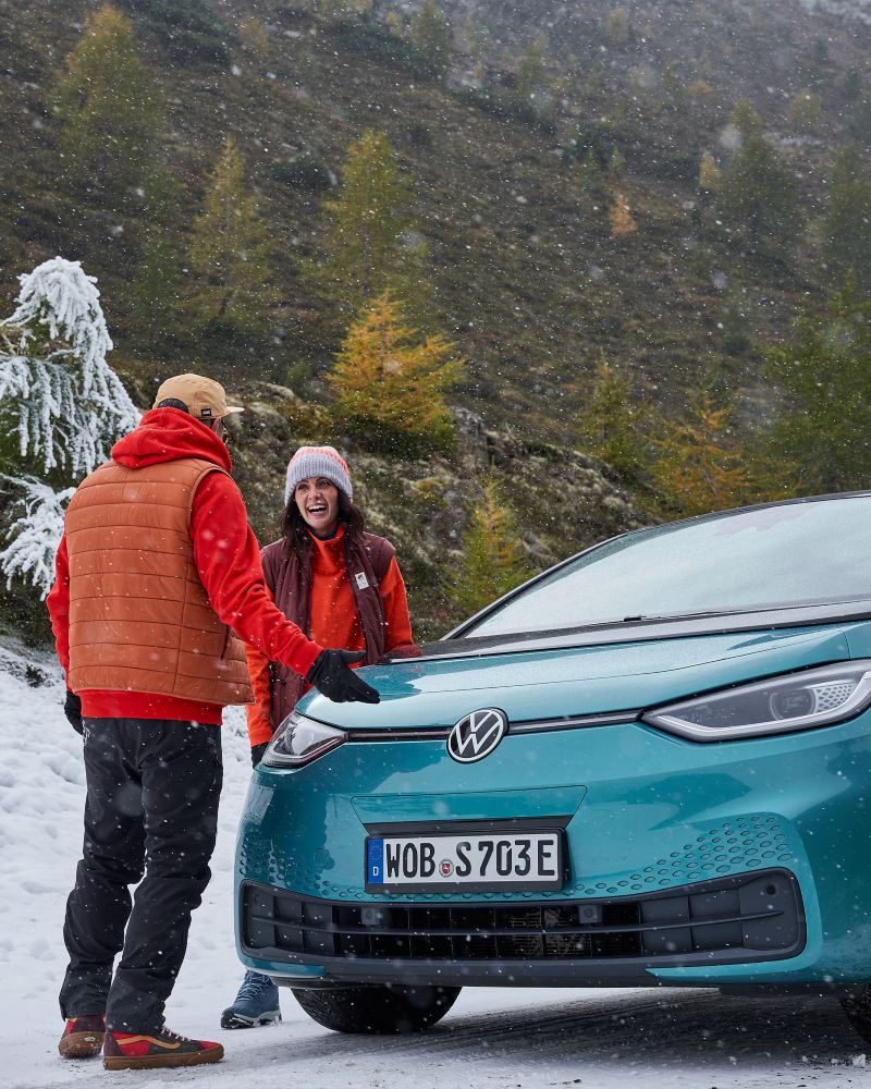 Ein Pärchen an einem verschneiten Berghang, daneben ein VW ID.3 1st