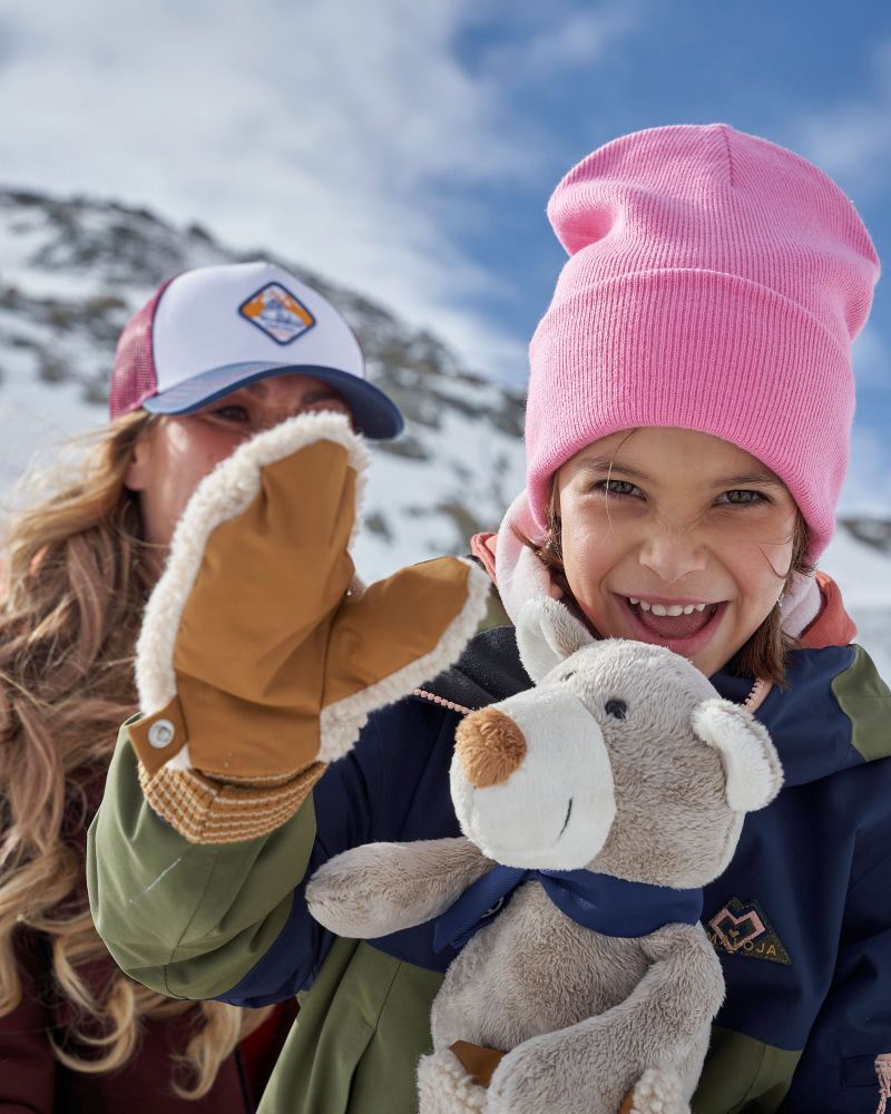 Mutter und Tochter im Schnee – das Mädchen mit Kuscheltier winkt in die Kamera