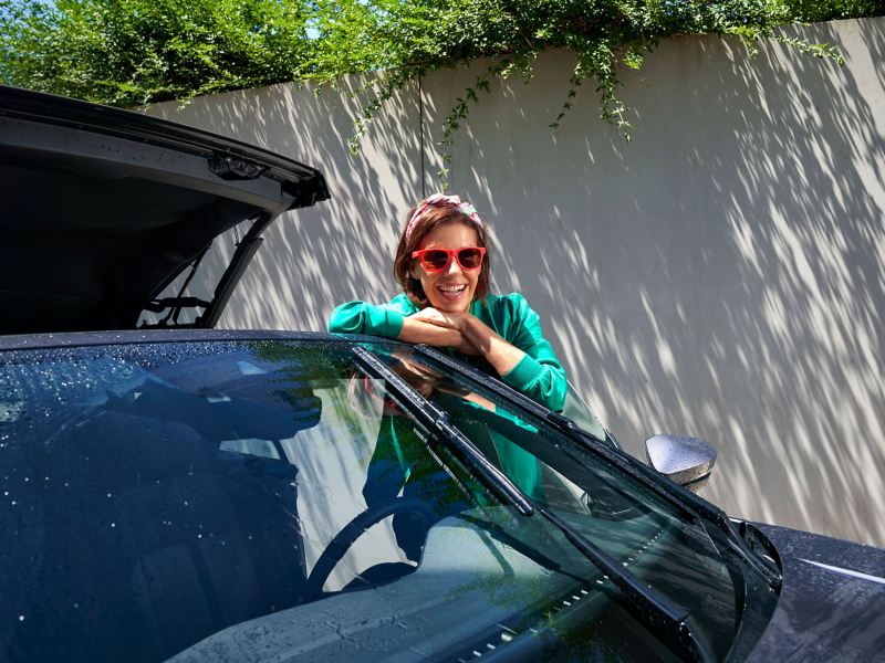Eine Frau lehnt glücklich an ihrem VW Auto mit offenem Verdeck