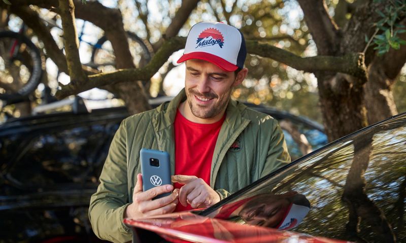 Man with cap looking at a smartphone, next to it a VW ID. vehicle