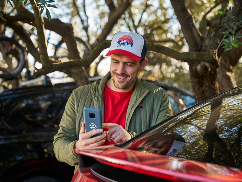 Un hombre con gorra mirando un smartphone, a su lado un vehículo VW ID.