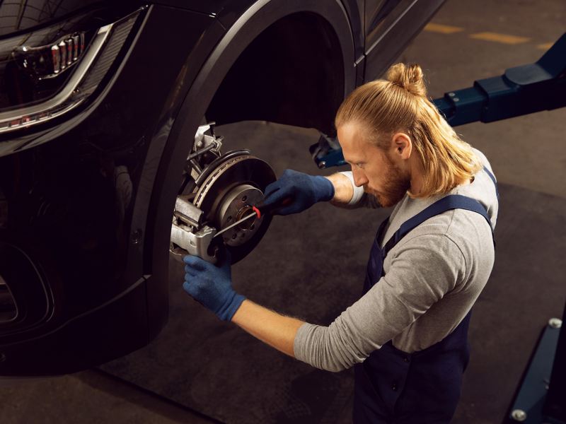 Ein VW Servicemitarbeiter prüft den Verschleiß an einer Bremse – Wartung und Verschleiß