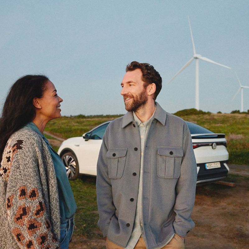 Mann und Frau  unterhalten sich, im Hintergrund VW ID.5 und Windräder – Way to Zero von Volkswagen