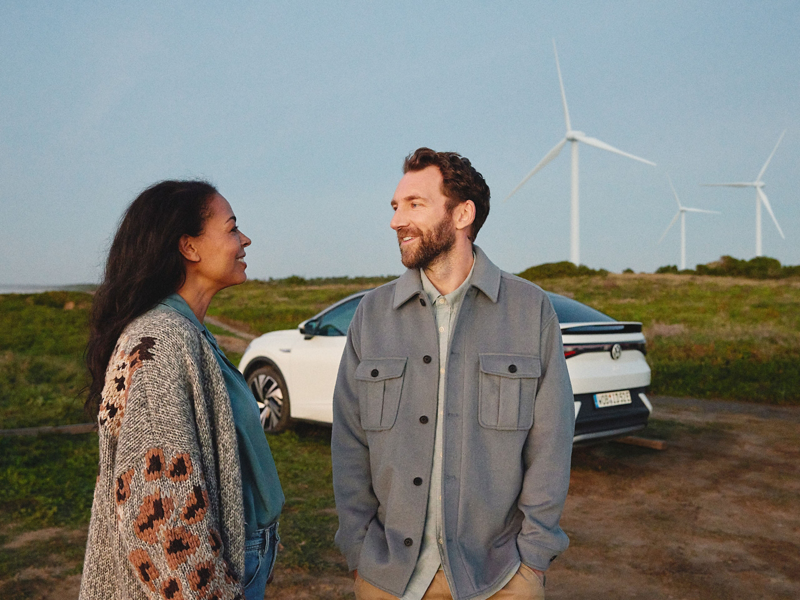 Mann und Frau  unterhalten sich, im Hintergrund VW ID.5 und Windräder – Way to Zero von Volkswagen