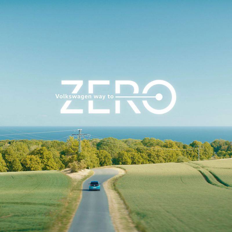 Ein elektrisches VW Auto fährt auf einer Straße in die Natur, darüber der Text: Way to Zero
