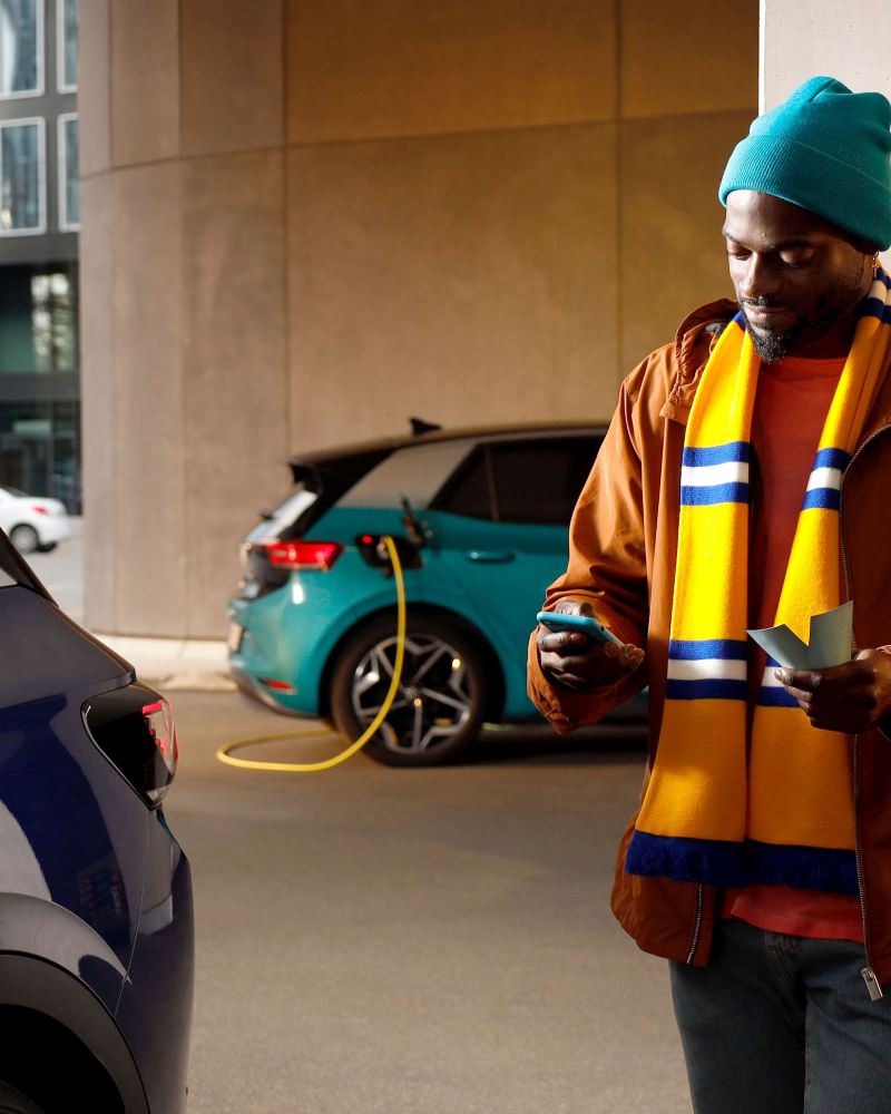 Ein Mann startet den Ladevorgang seines Elektroautos mit der Volkswagen App, ein VW ID.3 wird im Hintergrund geladen