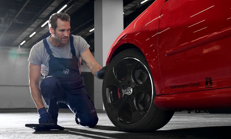 Un employé du service Entretien VW examine le pneu d’une VW rouge – connaissance des roues