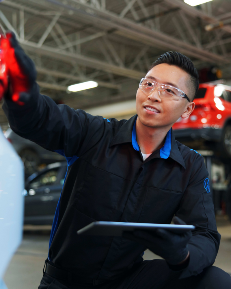 Certified VW technician inspecting exterior of VW vehicle.