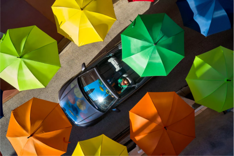 Convertible VW driving among colorful umbrellas.