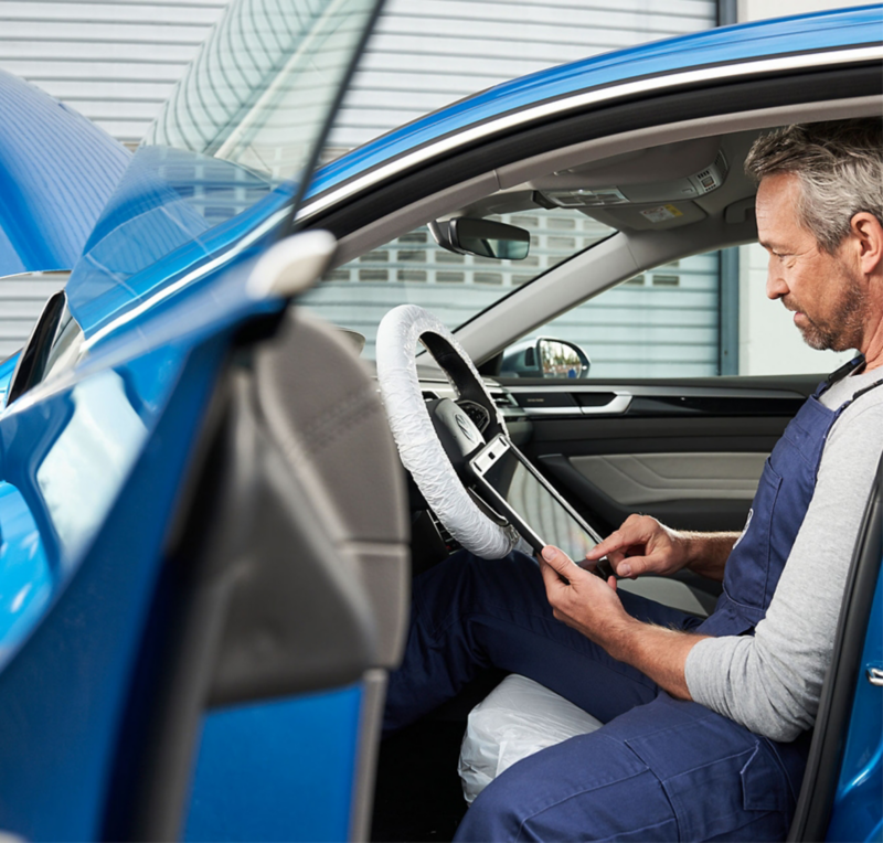 Certified VW technician inspecting blue vehicle.