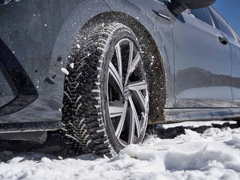 Dettaglio di uno pneumatico invernale di una vettura Volkswagen su una strada ricoperta di neve.