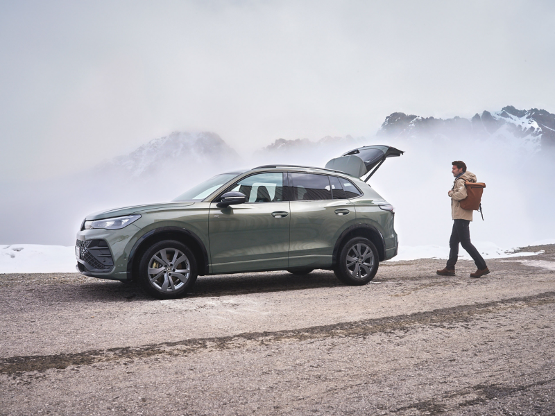 VW Tiguan im Nebel, Mann mit Rucksack geht auf geöffneten Kofferraum zu