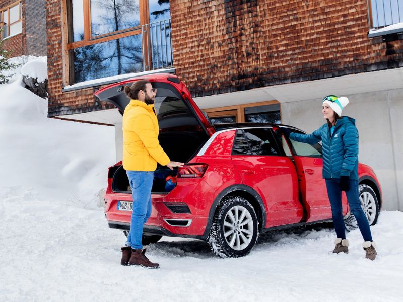 Ein Mann und eine Frau stehen im Winter an ihrem roten VW T-Roc mit VW Winterreifen