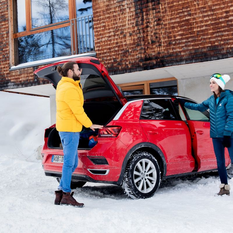 Ein Mann und eine Frau stehen im Winter an ihrem roten VW T-Roc mit VW Winterreifen