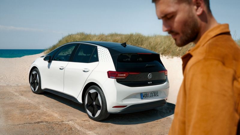 Hombre mirando al suelo con un Volkswagen ID.3 blanco de fondo aparcado en la playa