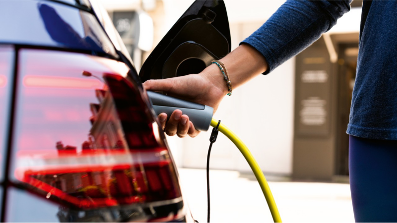 Mano sujetando el enchufe de carga eléctrica conectado a un vehículo de Volkswagen