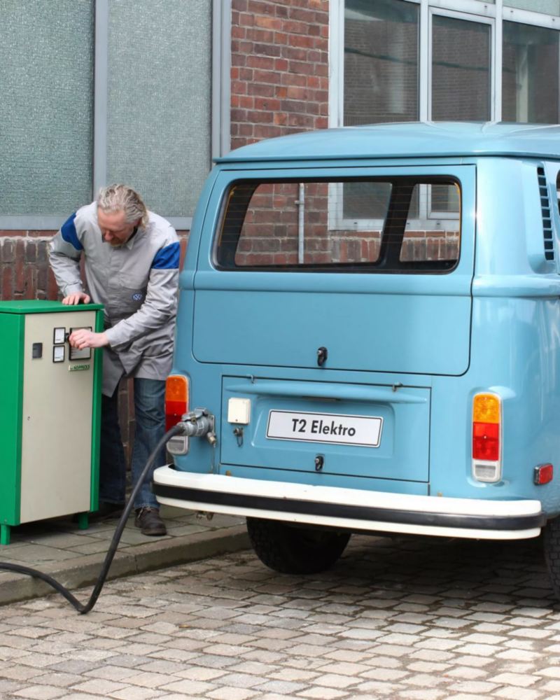 Hombre cargando una furgoneta eléctrica retro azul celeste de Volkswagen en la ciudad