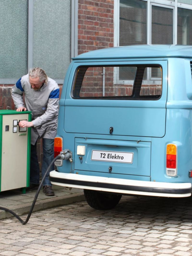 Hombre cargando una furgoneta eléctrica retro azul celeste de Volkswagen en la ciudad