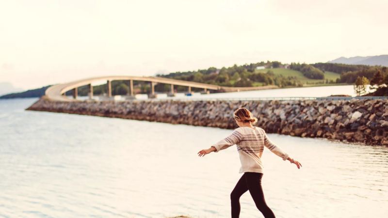 Chica andando con los brazos en alto por las rocas en la orilla del mar al atardecer