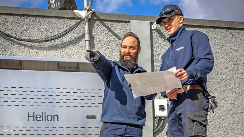 Zwei Handwerker besprechen sich, im Hintergrund das Helion Logo