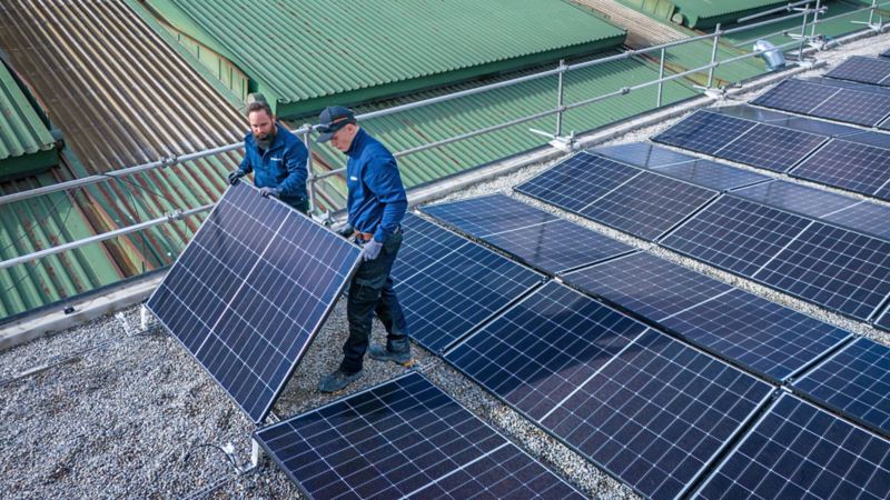 Deux artisans installent des panneaux solaires sur le toit de la Yakin Arena.