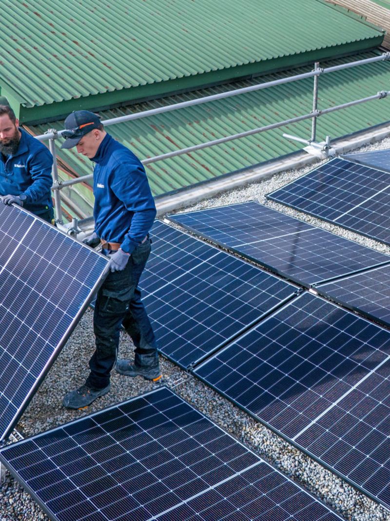 Deux artisans installent des panneaux solaires sur le toit de la Yakin Arena.