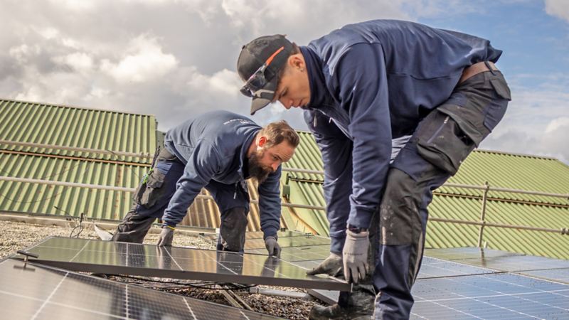 Deux ouvriers installent des panneaux solaires sur le toit de la Yakin Arena