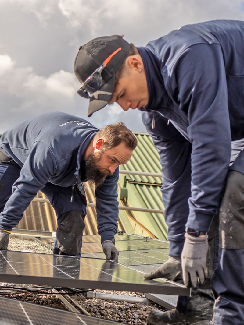 Due artigiani installano i pannelli solari sul tetto della Yakin Arena