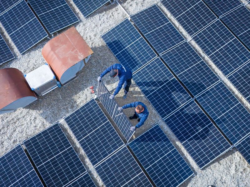 Deux ouvriers installent des panneaux solaires sur le toit de la Yakin Arena