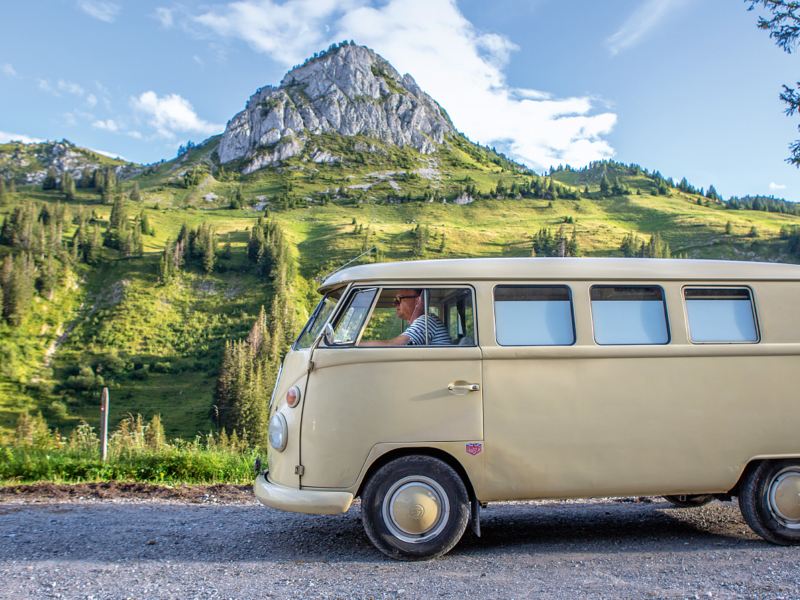 Bulli ist auf einem Feld parkiert und Berge sind im Hintergrund