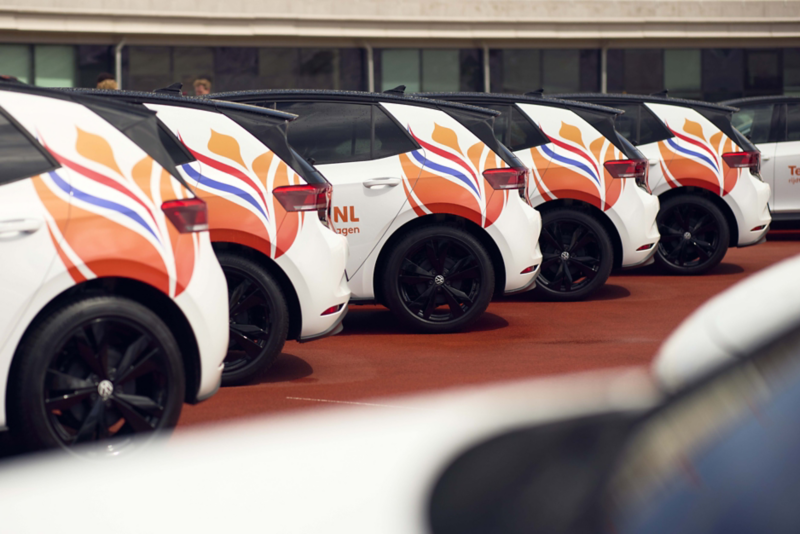 TeamNL sporter staat achter een ID.3, hij heeft een wiel vast van een fiets die achterop de ID.3 staat, hij heeft een oranje jasje aan