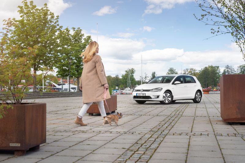 Kvinna med hund framför en VW e-Golf