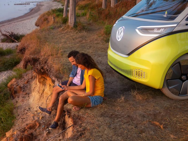 Couple sitting by electric vehicle looking at ocean.